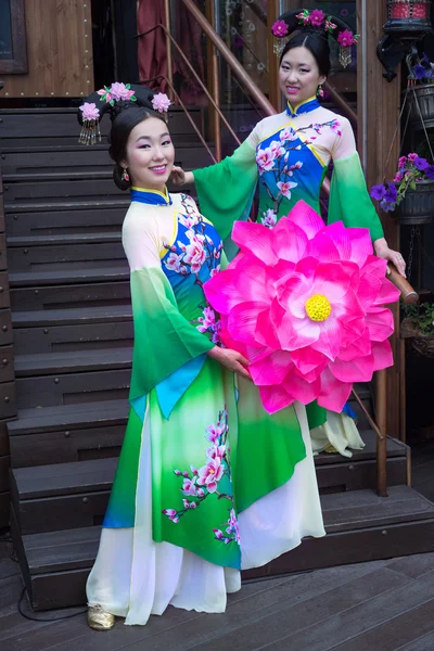 Twee Aziatische meisjes in traditionele Chinese jurken met paraplu in de vorm van lotusbloemen staande op de trap — Stockfoto
