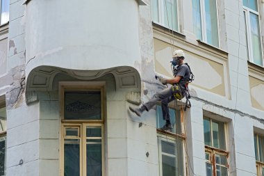 worker alpinist in a protective mask working with sander for smoothing wall surface of the building clipart