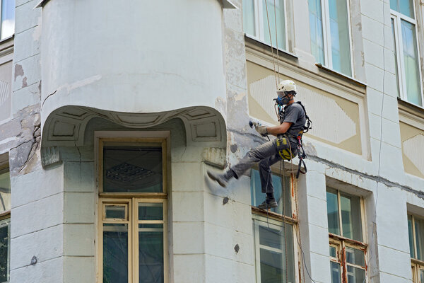 worker alpinist in a protective mask working with sander for smoothing wall surface of the building