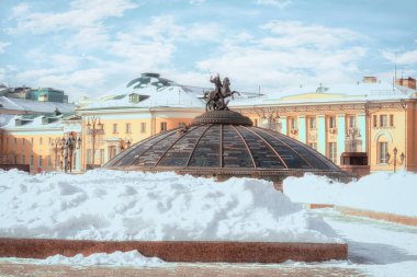 Snow pile at Manege Square. Glass cupola crowned by a statue of Saint George, holy patron of Moscow. (Inscription in Russian: names of famous cities in the world). Winter in Moscow, Russia.