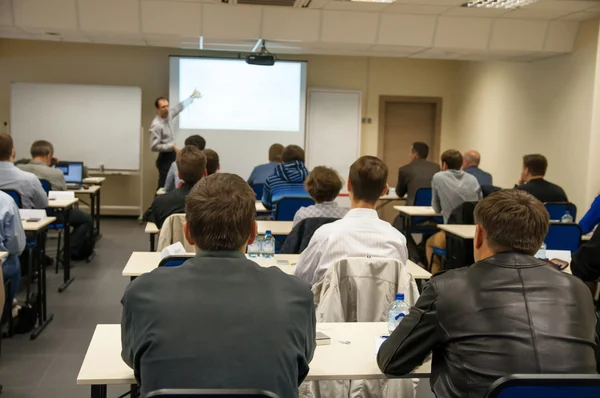 Visão traseira das pessoas sentadas na aula à mesa e ouvindo a apresentação — Fotografia de Stock