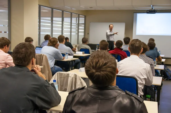 Rear view of the people sitting in the class by the table and listening the presentation — Stock Photo, Image