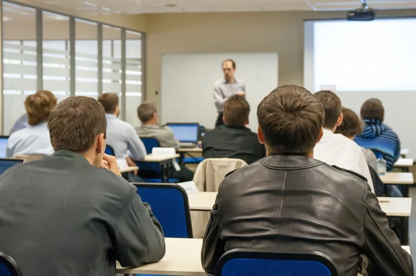 Rear view of the people sitting in the class by the table and listening the presentation — Stock Photo, Image
