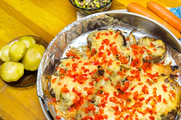 Frying meat under the cheese laying on a round metall dish on a folio, pickled scallops on the plate and carrots on a wooden table — Stock Photo, Image