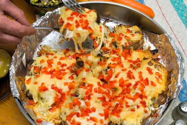 Frying meat under the cheese laying on a round metall dish on a folio, and an arms with forks carrying the piece of the dish — Stock Photo, Image