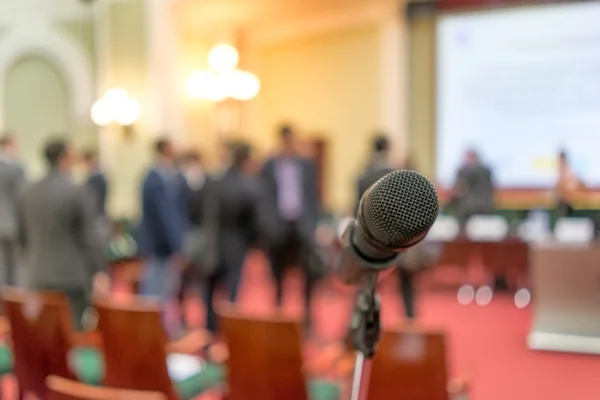 Microphone in focus against blurred chairs and standing talking audienc