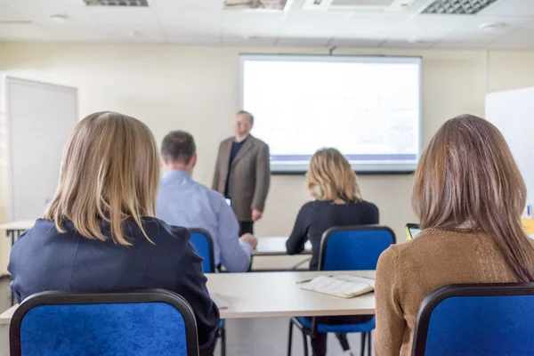 People sitting rear at the desks in the education class and the lecturer near the white desk