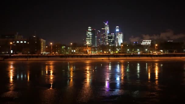 Москва река течет вода в ночное время и центр Москвы освещается и улица с движущимися автомобилями на размытие за кулисами . — стоковое видео