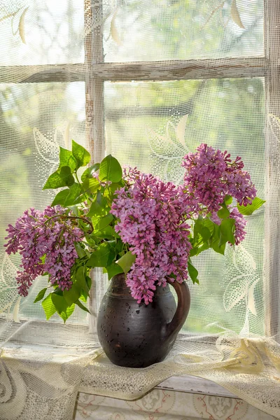 Lush bouquet of lilac in a brown clay vase on a window sill — Stock Photo, Image