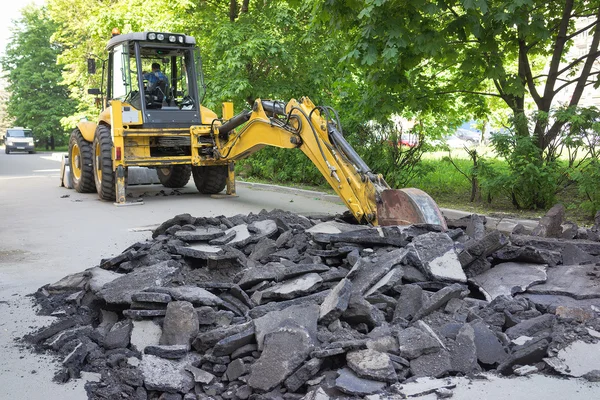 Жовтий сучасний екскаватор прибирає сміття асфальтованої дороги в місті — стокове фото