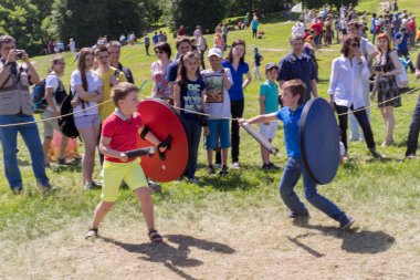 MOSCOW, RUSSIA - JUNE 07, 2015: two boys fighting with a wooden swords and shields playing knights on the park in a sunny day in Moscow