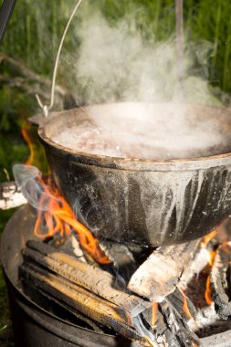 Cooking soup in a pan over campfire.