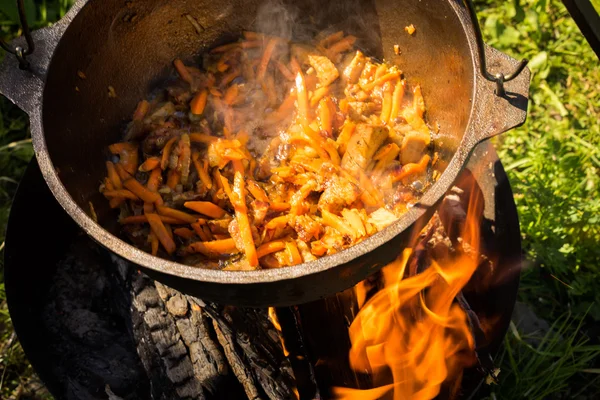 Close up view of cooking meat, onion and carrot in a metal pan in a campfire — Stock Photo, Image