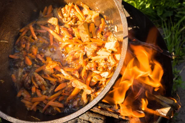 Close up view of cooking meat, onion and carrot in a metal pan in a campfire — Stock Photo, Image