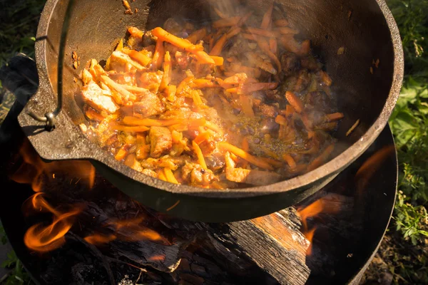 Close up view of cooking meat, onion and carrot in a metal pan in a campfire — Stock Photo, Image