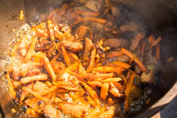 Vista de perto de cozinhar carne, cebola e cenoura em uma panela de metal em uma fogueira — Fotografia de Stock