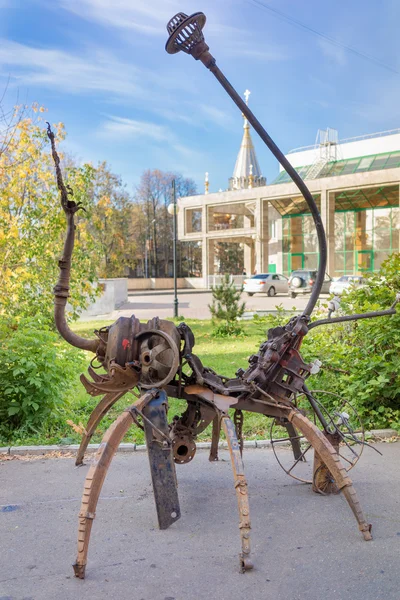 Izhevsk, Russia - September 16, 2015: Scrap metal modern sculpture on the street of the town, Kalashnikiv museum and the St. Michael cathedral on the backstage. — Stock Photo, Image