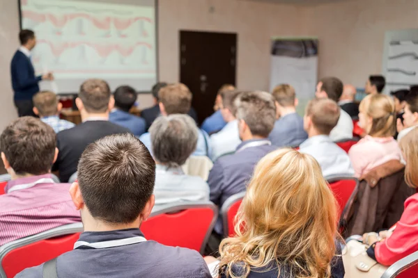 Achteraanzicht van mensen uit het bedrijfsleven luisteren aandachtig op conferentie. Presentator met verslag in de buurt van het scherm. — Stockfoto