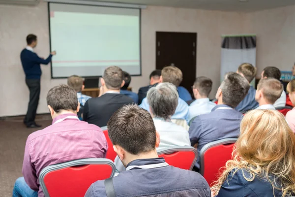 Conferentie publiek: mensen die zitten achter in de bedrijfskundige opleiding en de docent in de buurt van het whiteboard wijzend op het scherm — Stockfoto
