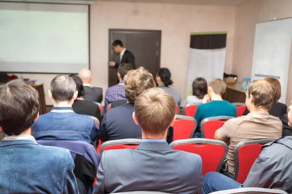 Speaker on the podium and rear view of the people at the conference hall. — Stock Photo, Image