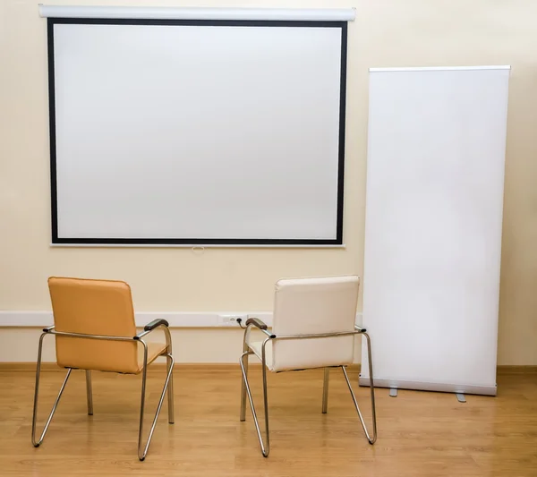 Blank white screen and roll-up banner and two chairs — Stock Photo, Image
