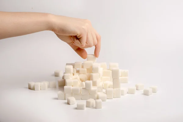 Un bras construisant des cubes de sucre dans une pile sur fond blanc — Photo