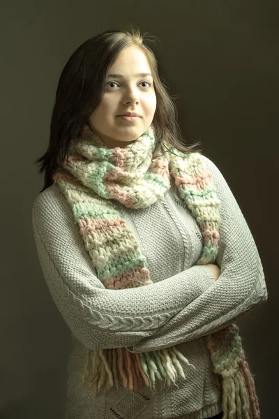 Cheerful young female in winter knitted sweater and scarf posing with arms crossed on dark grey background — Stock Photo, Image