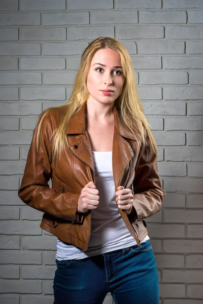 Young elegant blond woman in a leather jacket in front of brick wall backround — Stock Photo, Image