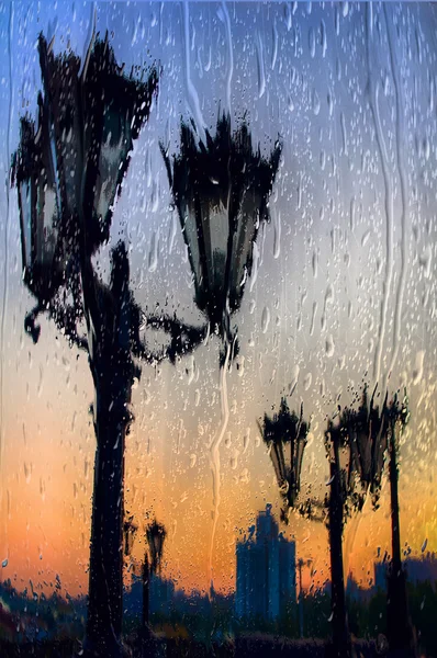 Città di Ekaterinburg gettare le sagome dei lampioni, vista attraverso il vetro bagnato in un tramonto piovoso — Foto Stock
