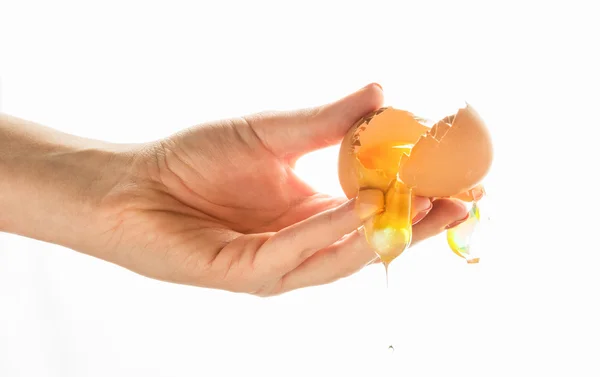 手打破一个鸡蛋。鸡蛋蛋黄滴下来，落在白色的背景. — 图库照片