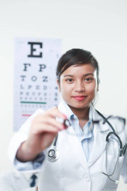 Arkasında steteskop ve görüş tablosu olan bir kadın doktor.