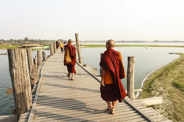 MANDALAY, MYANMAR - FEB 14: Monks walk on U Bein Bridge where is the oldest and longest teak wooden bridge in the world — стоковое фото