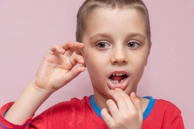 Sevimli ilkokul çocuğu kendi elleriyle süt dişini çekti. Düşen dişi tutuyor ve dişin yerini ağzında gösteriyor. Diş çekmek mi?.