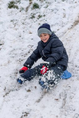 Plastik kızaklı çocuk karda oynuyor.