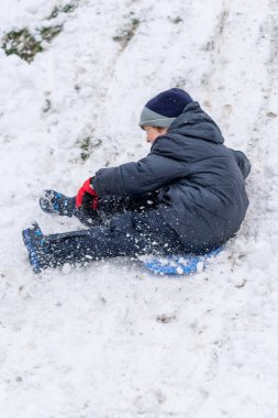 Plastik kızaklı çocuk karda oynuyor.