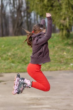 Gözlüklü, patenli bir kız. Mevsimlik açık hava çocuk aktivitesi sporu. Kız patenlerle zıplıyor.