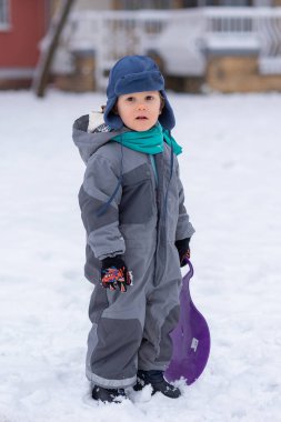 Plastik kızaklı çocuk karda oynuyor.