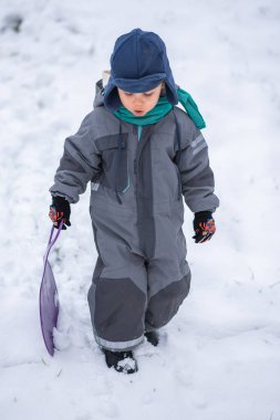 Plastik kızaklı çocuk karda oynuyor.