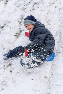Plastik kızaklı çocuk karda oynuyor.