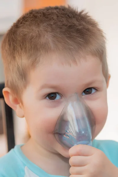 Little boy using nebulizer during inhaling therapy. Little boy making inhalation with nebulizer at home. Close up portrait of boy taking inhalation for asthma prevention.