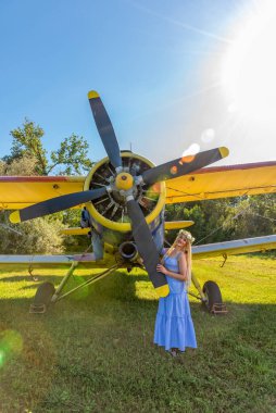 Güzel bir kadın bir uçağın yanında duruyor. Kafasında çiçek çelengi olan bir kadın.