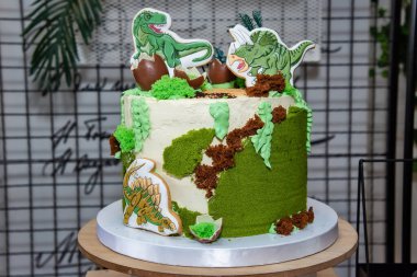 Bir dinozor doğum günü pastası. Dinozorlarla süslenmiş çocuk bayramı pastası Jurassic dönemi ormanında.