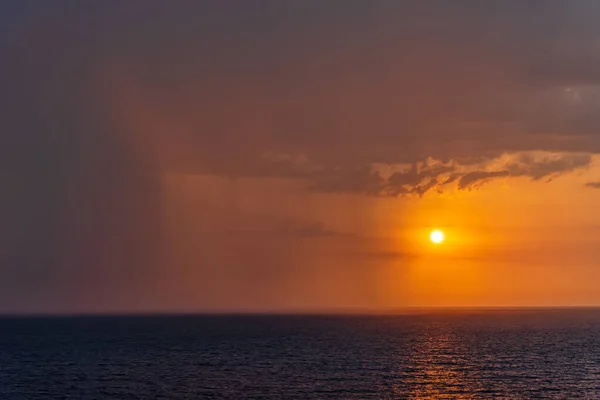 Sunset and rain at sea in the same photo. Sunlight and rainy clouds in the horizon at sea.