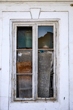 Eski, yıpranmış ahşap bir pencere. Pencere camında beyaz boya var. Alt camlar tahtayla kapatılmış. 