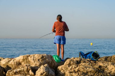 Malaga, İspanya - 06 Ağustos 2024: Bir adam kayalıklarda balık tutuyor.