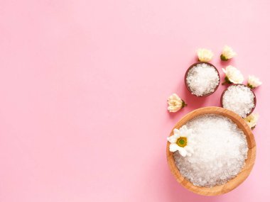 Spa yassı kompozisyonu. Kavanozlarda deniz tuzu, pembe arka planda çiçek. Kopyalama alanı, üst görünüm. Evde bakım kavramı, rahatla ve dinlen..