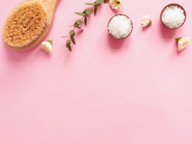 Spa yassı kompozisyonu. Kavanozlarda deniz tuzu, masaj ahşap fırça, bitki, pembe arka planda çiçek. Kopyalama alanı, üst görünüm. Evde bakım kavramı, rahatla ve dinlen..