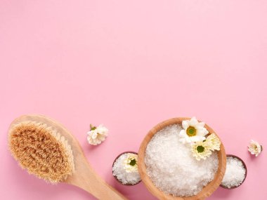 Spa yassı kompozisyonu. Kavanozlarda deniz tuzu, masaj ahşap fırçası, pembe arka planda çiçek. Kopyalama alanı, üst görünüm. Evde bakım kavramı, rahatla ve dinlen..