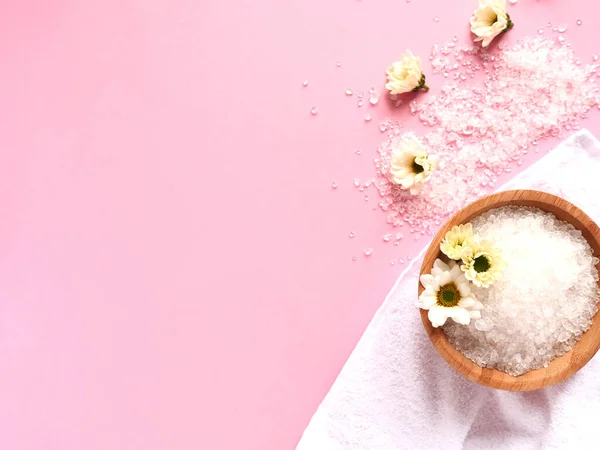 Spa yassı kompozisyonu. Serpilmiş ve kavanozda deniz tuzu, banyo havlusu, pembe arka planda çiçek. Kopyalama alanı, üst görünüm. Ev bakımı kavramı.