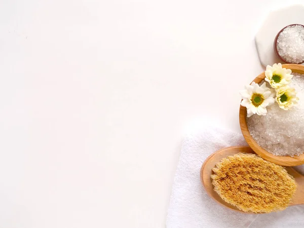 Spa yassı kompozisyonu. Deniz tuzu, banyo havlusu, masaj ahşap fırçası, beyaz arka planda çiçek. Kopyalama alanı, üst görünüm. Evde bakım kavramı, rahatla ve dinlen..